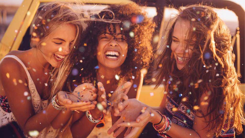 Three joyful women celebrating with confetti, embodying a vibrant and purposeful culture, reflecting the themes of community and intentional experiences from *Culture by Design*.