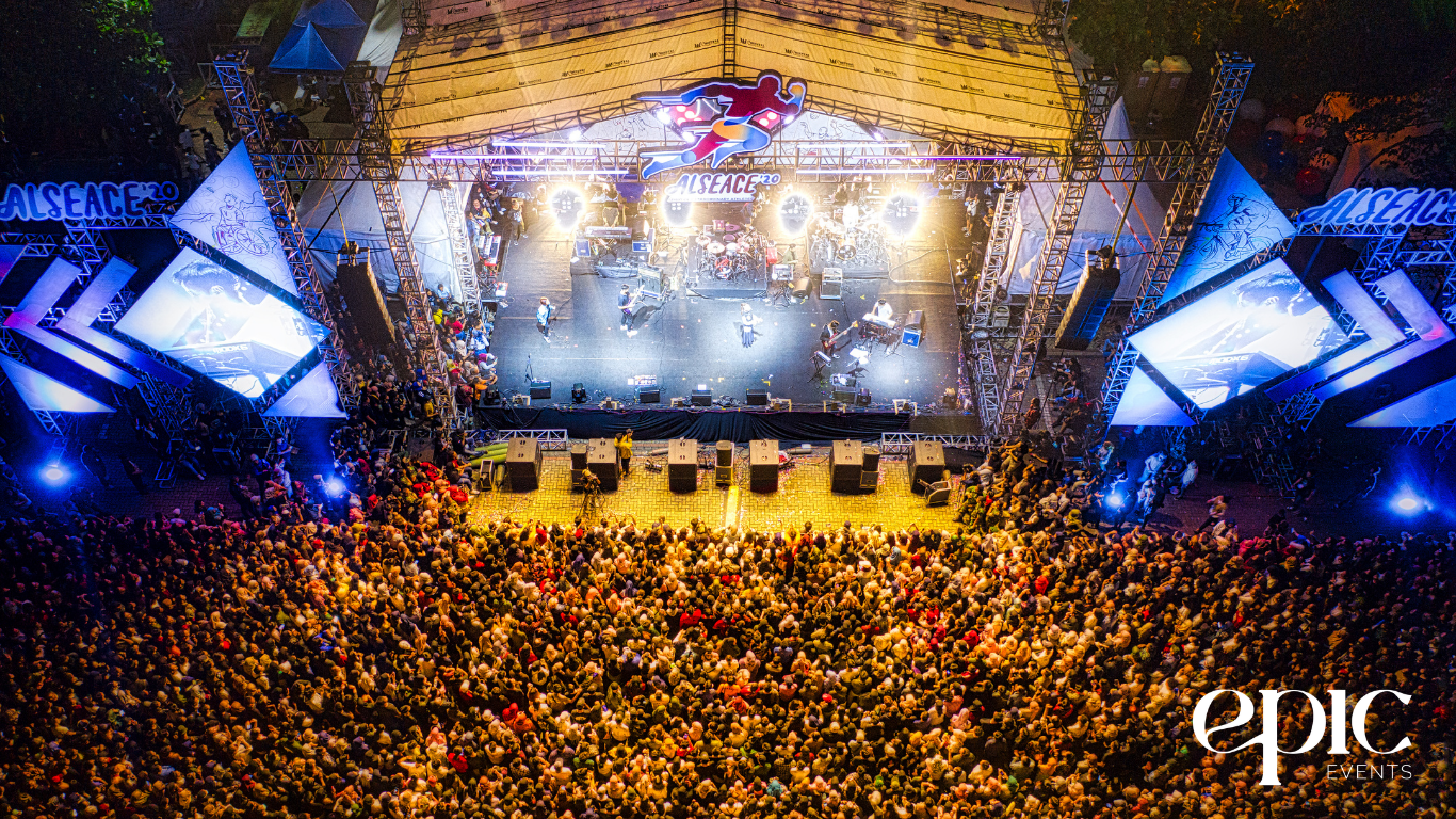 Crowd at a large outdoor event with a stage featuring performers, illuminated by bright lights, showcasing the importance of immersive experiences in event planning.